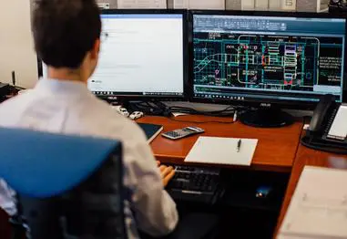 A man sitting at his desk looking at two computer screens.